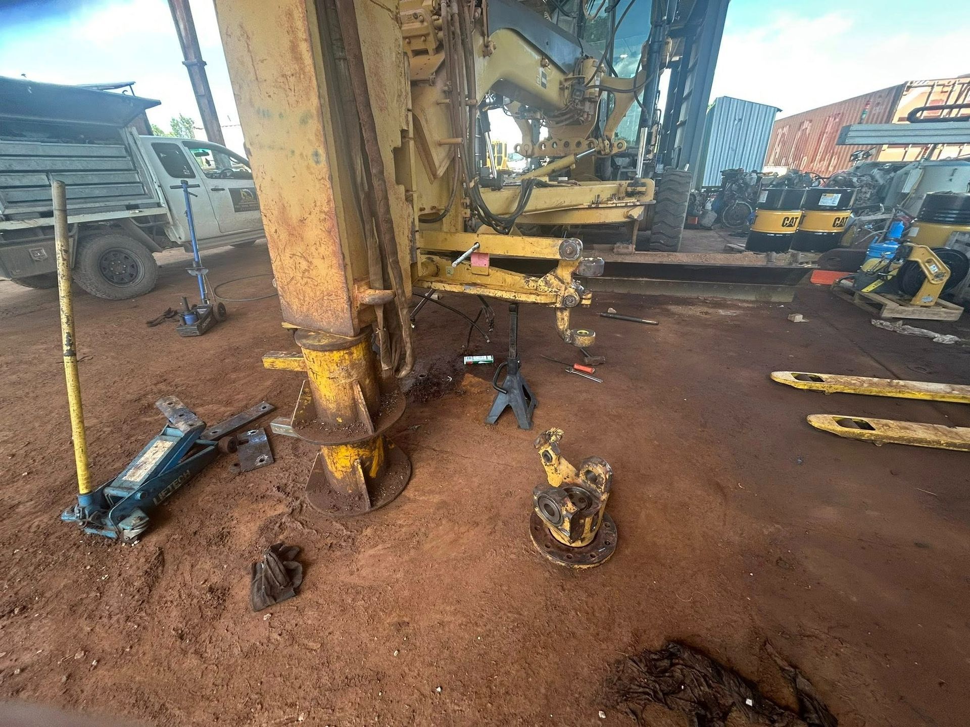 A yellow excavator being worked on in a dirt lot, with jacks and parts scattered around — Full Noise Mechanical in Humpty Doo, NT