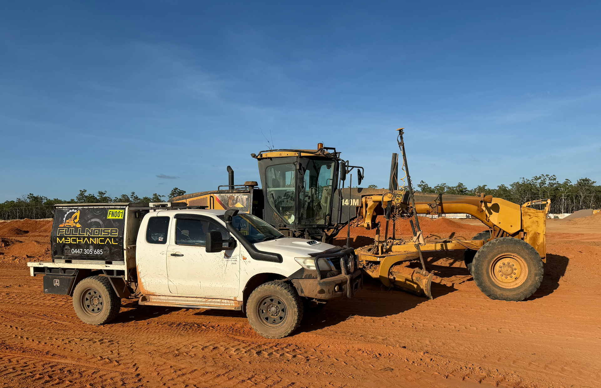 White pickup truck and yellow grader on a red dirt field under a blue sky — Full Noise Mechanical in Humpty Doo, NT