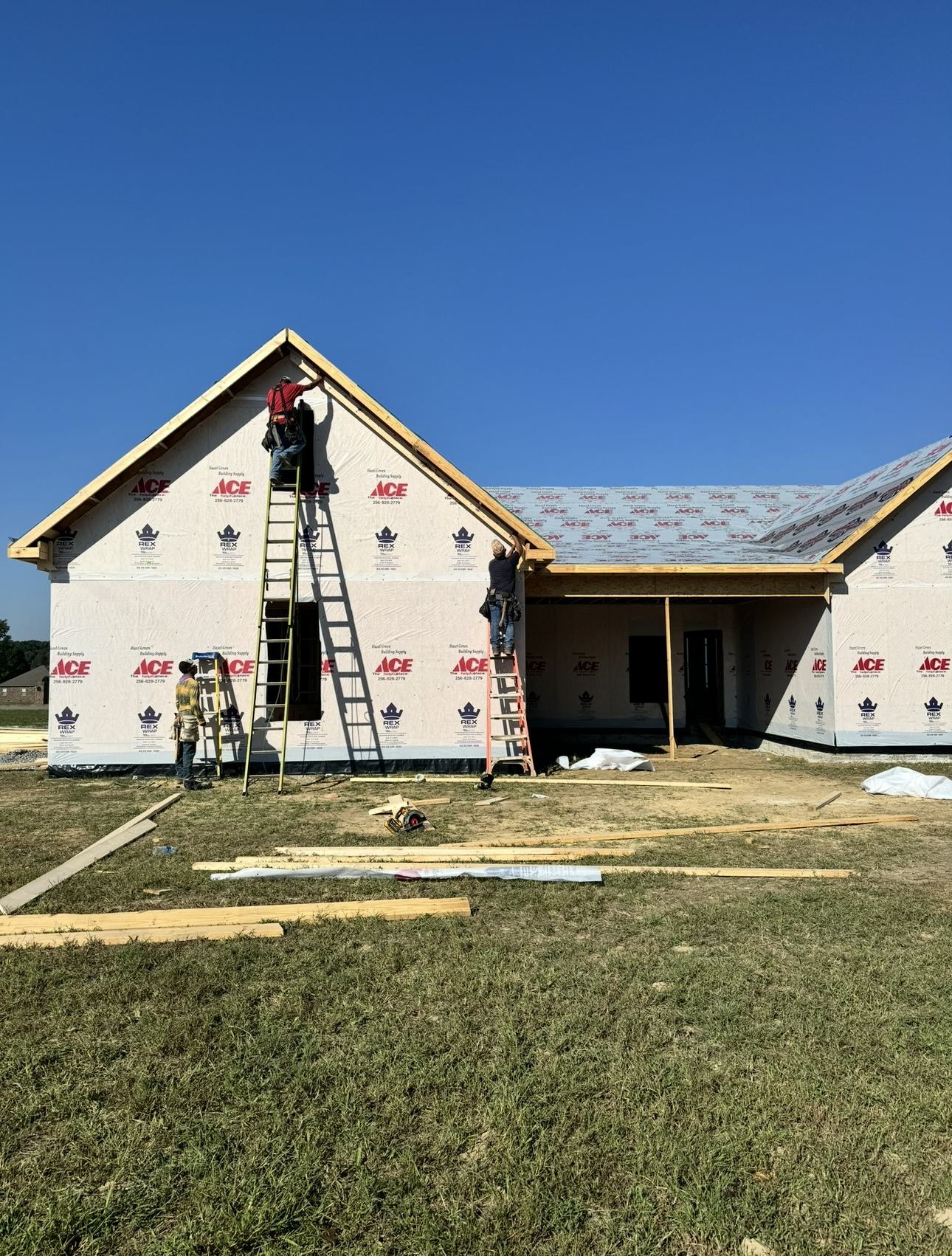 Single-story house under construction with exposed roof, blue sky, and grass in front