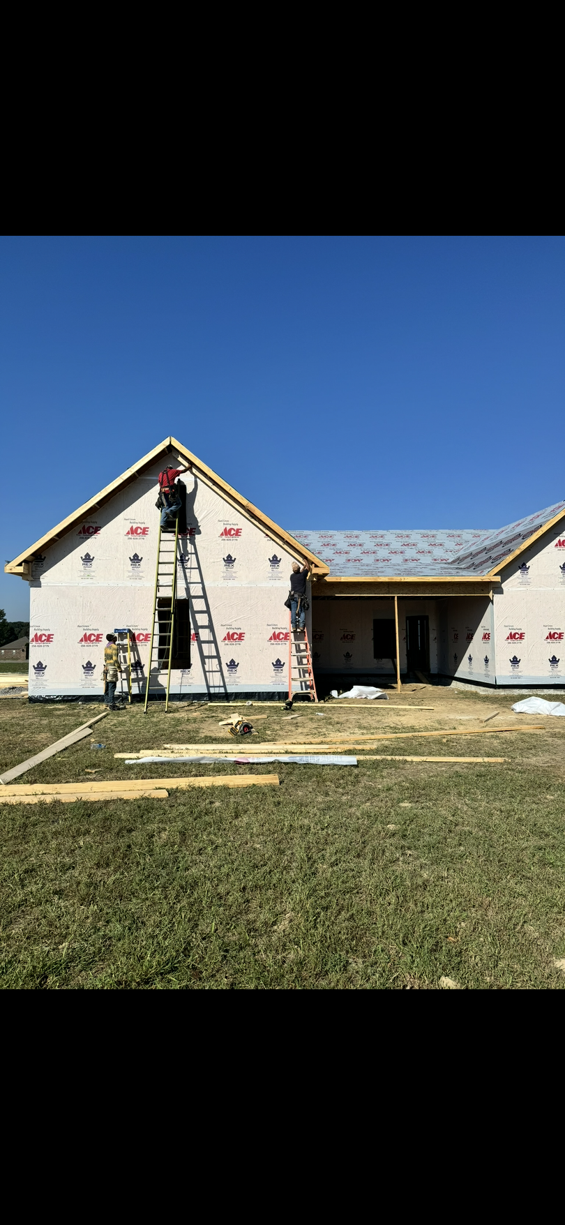 Partially built house with white walls, exposed framing, and a ladder under a clear blue sky