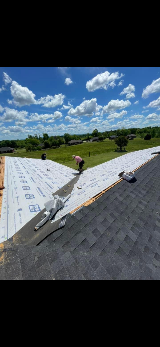 Worker installing roofing shingles on a sloped roof under a bright blue sky
