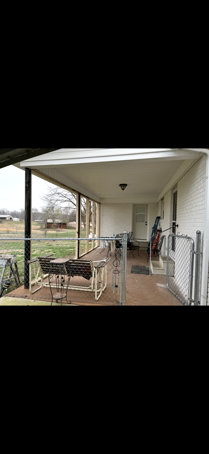 Covered patio with wicker seating, a table, and a view of the garden and fields beyond