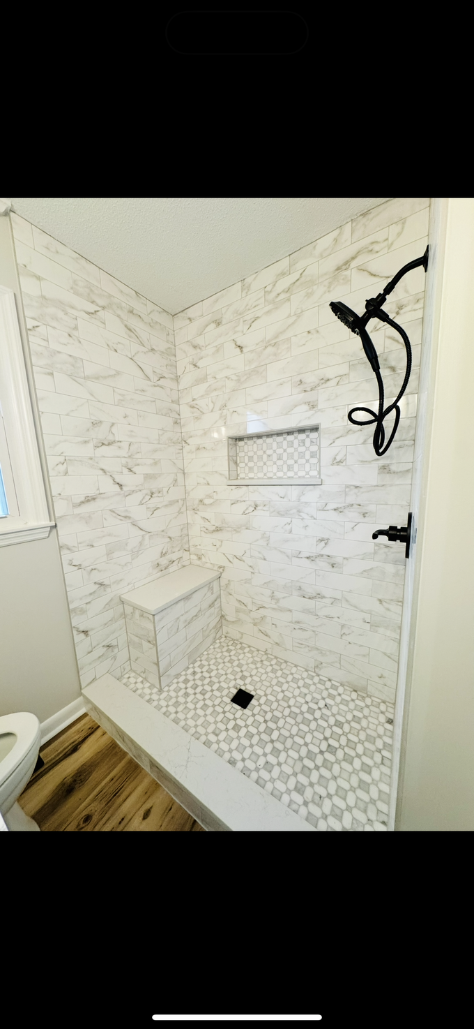 Small tiled shower with a black handheld showerhead and white walls.