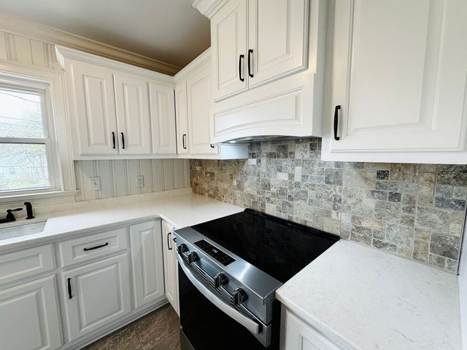 Bright kitchen with white cabinets, marble counters, and stainless steel stove with mosaic tile backsplash