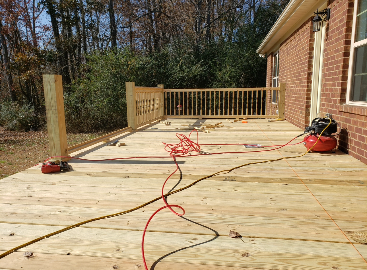 Wooden deck under construction beside a brick house, with tools and cords on the boards.