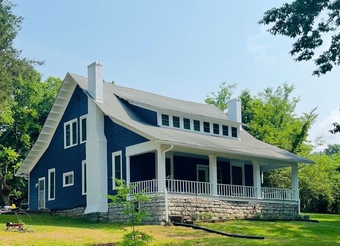 Blue house with white trim and wraparound porch on a sunny green lawn