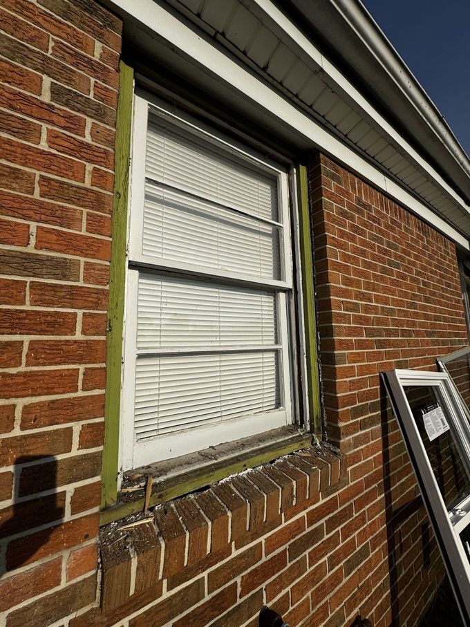 Brick house exterior with a white window and brick ledge, shot from below at an angle
