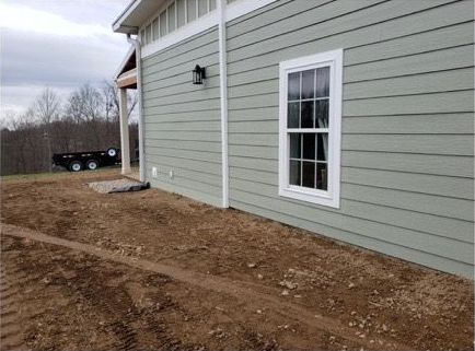 Worker applying stucco around a garage door on a house exterior, with ladders and tools nearby