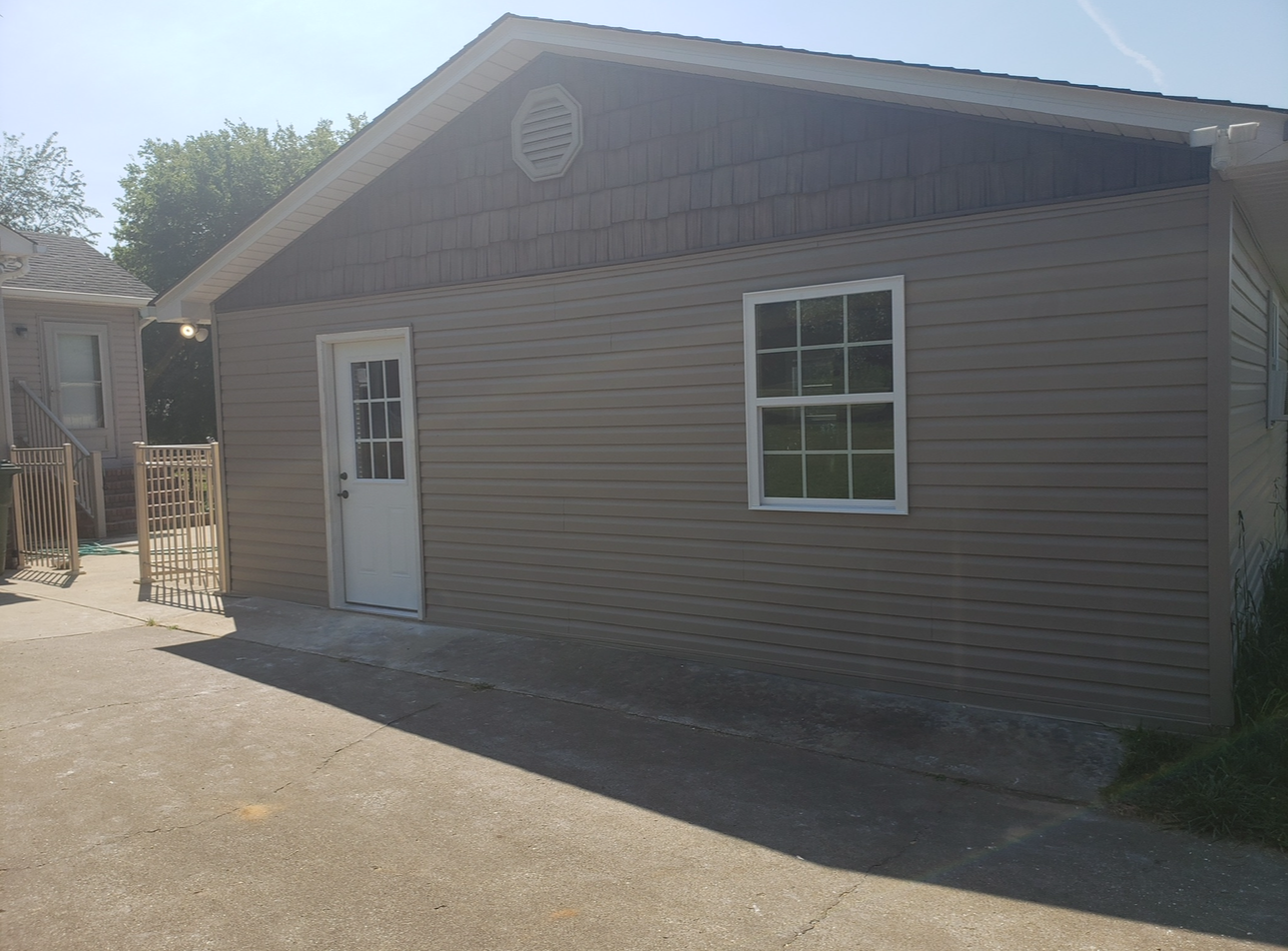 White stucco house with black-trimmed windows and a small porch, shown from the corner.