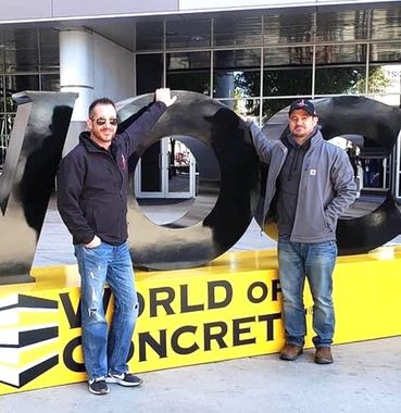 Two men standing in front of a sign that says world of concrete
