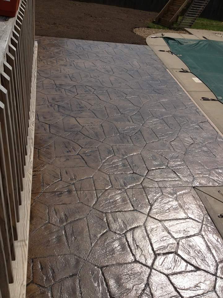 A concrete walkway next to a pool with a fence in the background