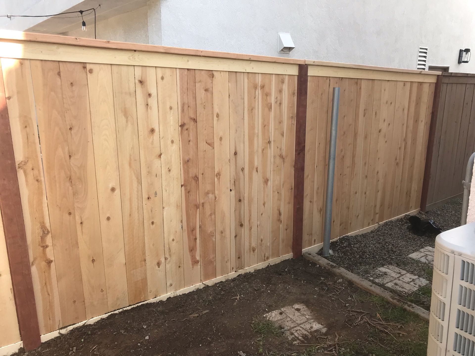 A wooden fence is sitting in a backyard next to an air conditioner.