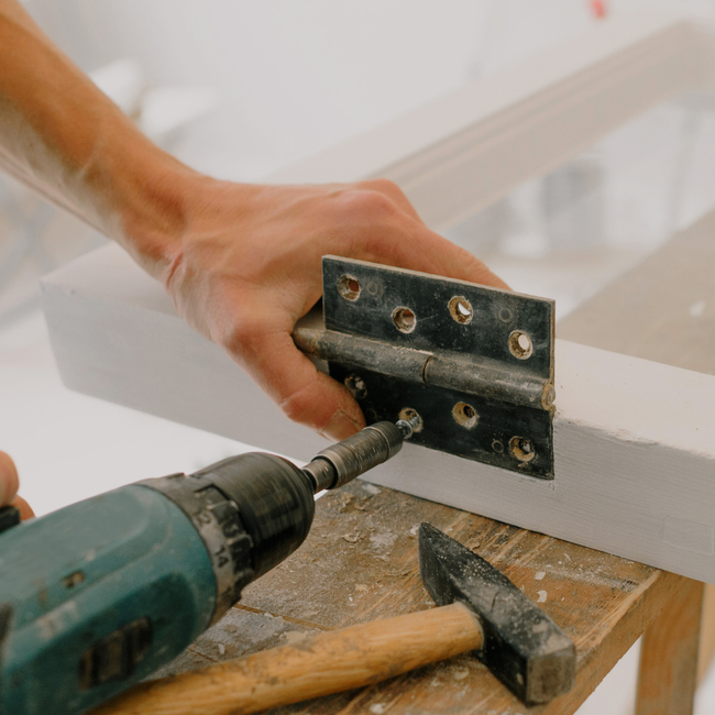 A person is using a drill to fix a door hinge.