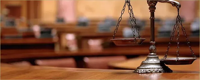 A scale of justice is sitting on a wooden table in a courtroom.