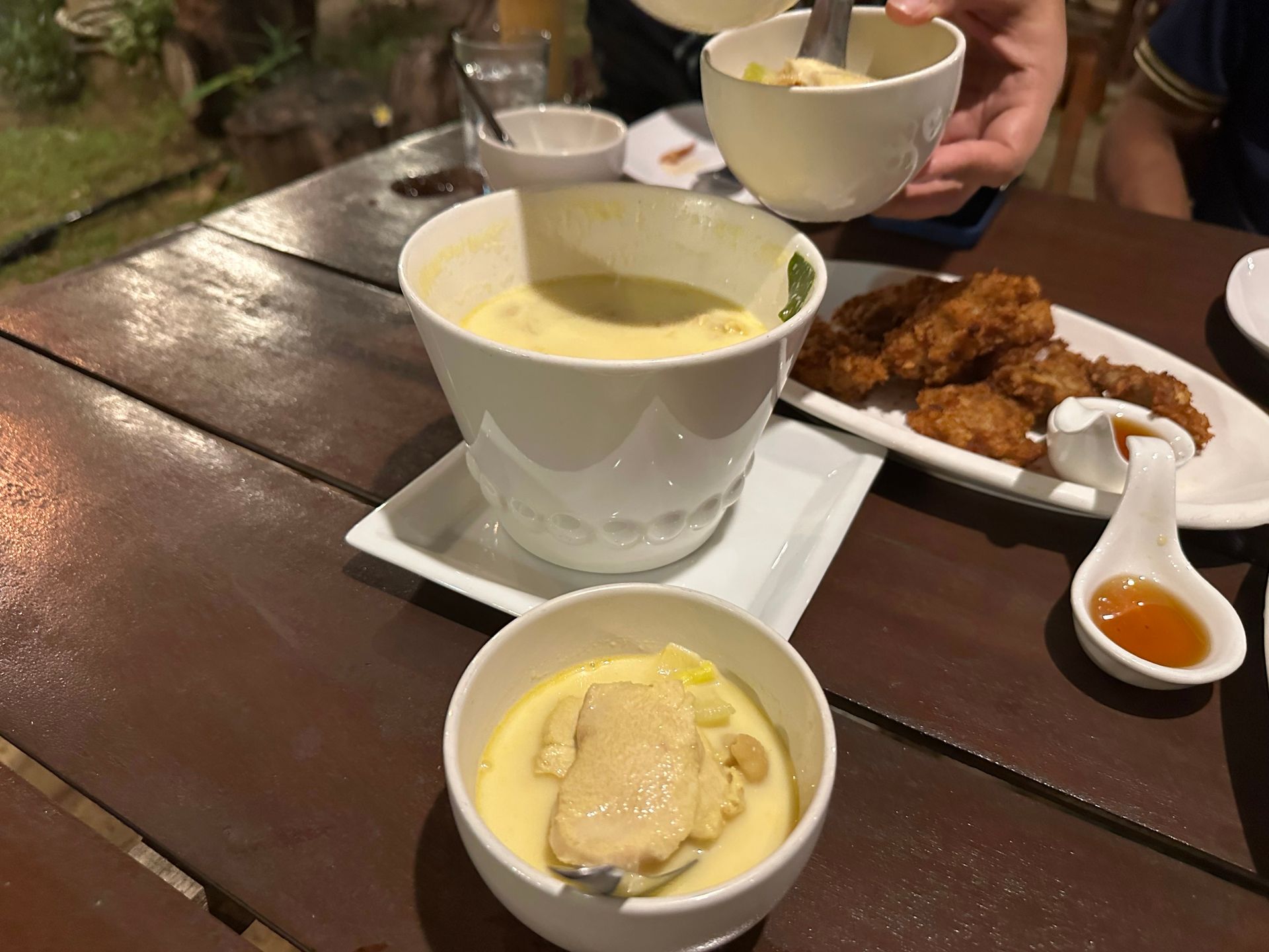 Soup, fried chicken, and dipping sauce on a wooden table at a restaurant.