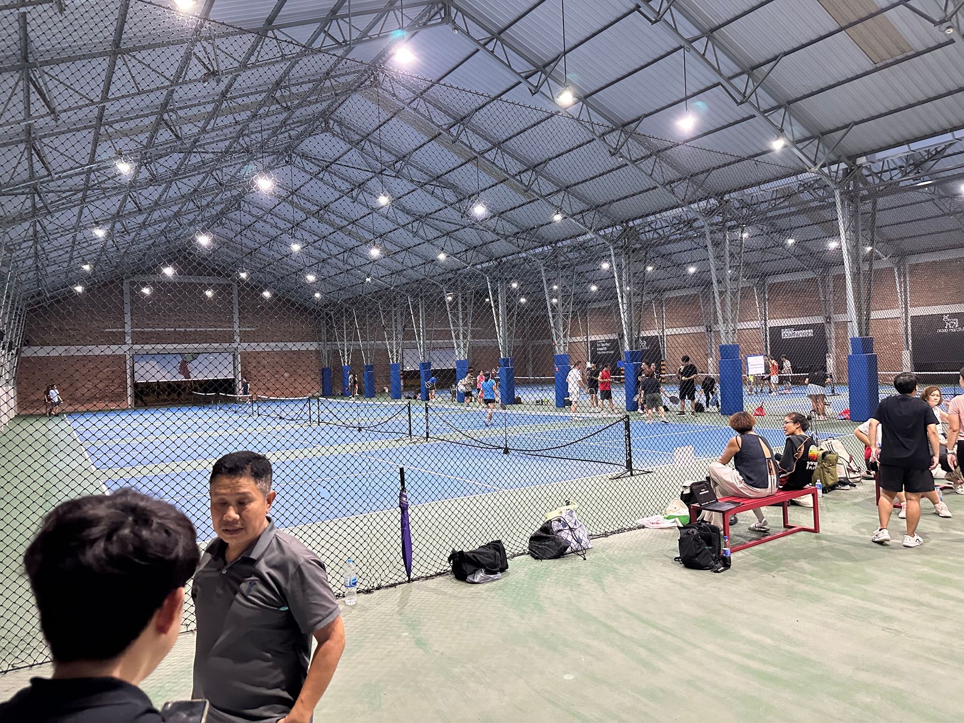 Indoor sports arena with people playing and watching a racket game behind a net under bright lights