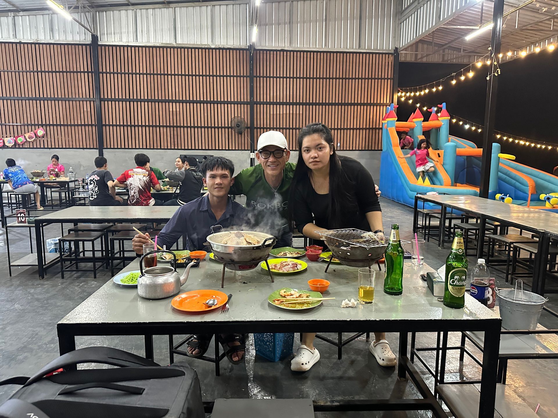 Three people seated at a dining table with food and drinks at an outdoor party setup