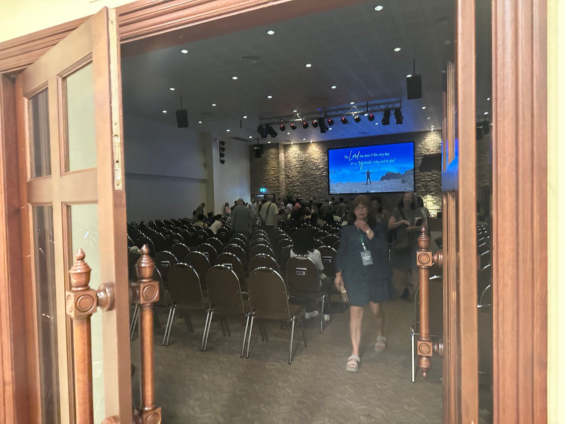 Open doorway to a conference hall with rows of chairs and a stage with a large screen.