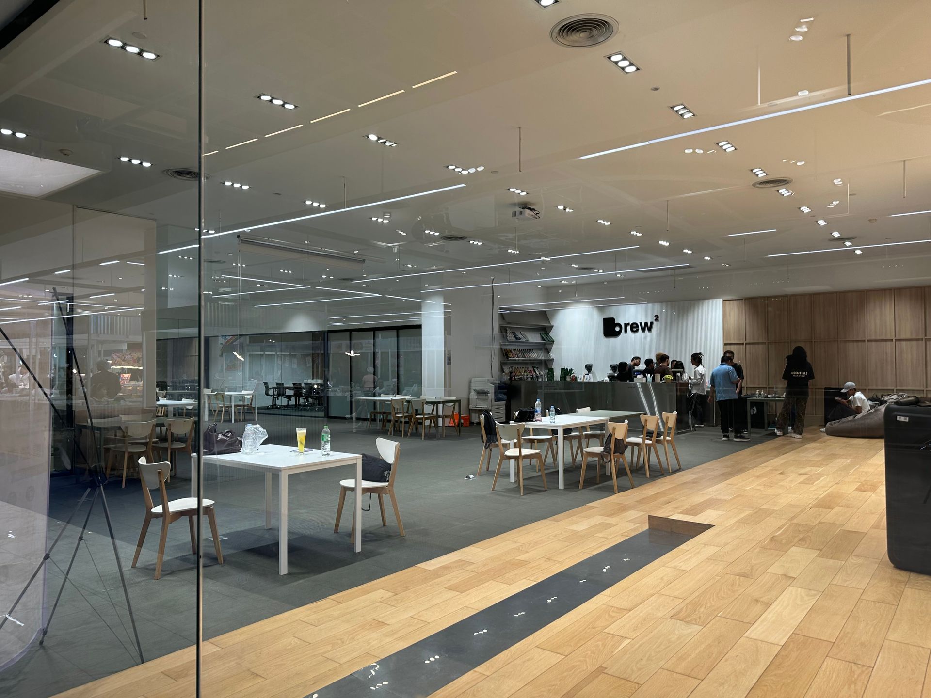 Modern glass-walled cafeteria with tables, chairs, and people seated inside