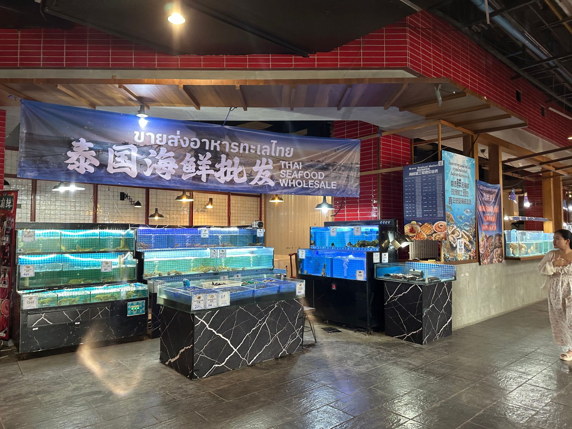 Seafood market stall with lit aquariums and Chinese sign inside a covered market.