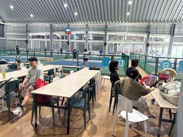 Indoor poolside seating area with people sitting at tables beside a large swimming pool.