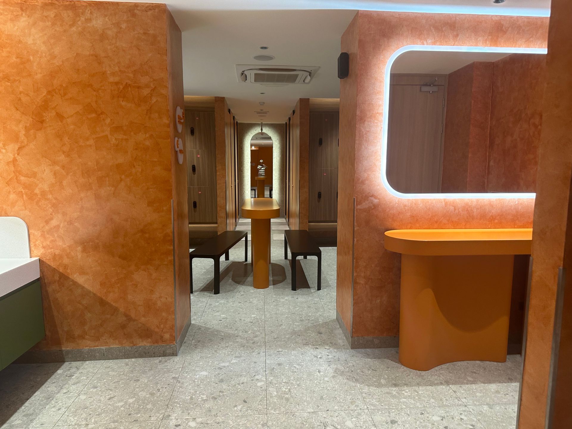 Orange-lit hallway with modern booths, mirrored center aisle, and a small counter on the right