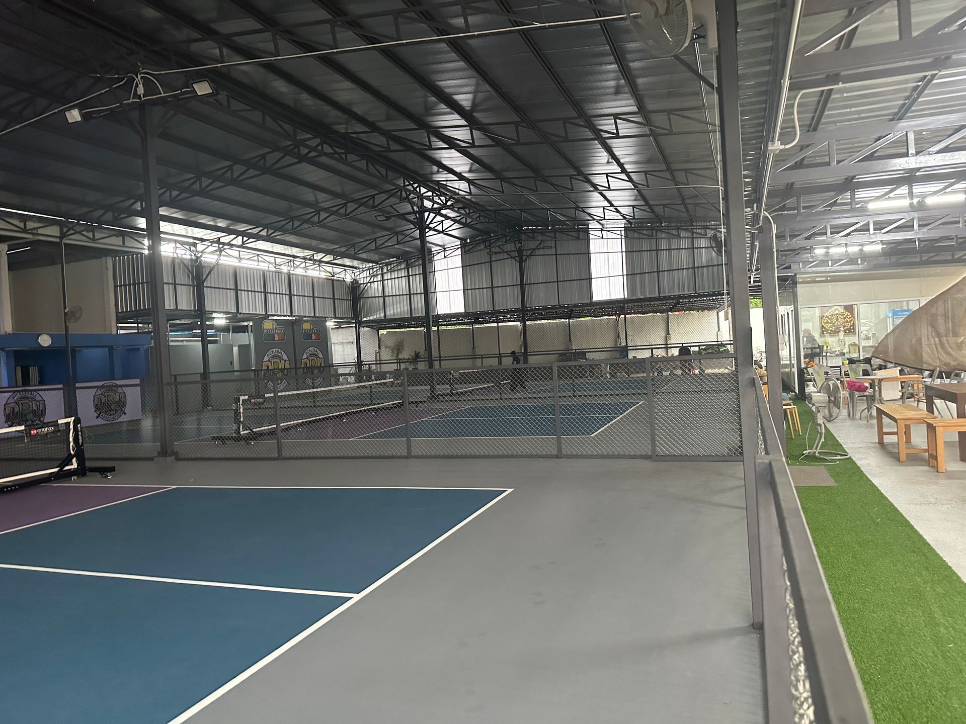 Indoor sports facility with blue court, netted enclosure, gray floor, and bleachers on the right