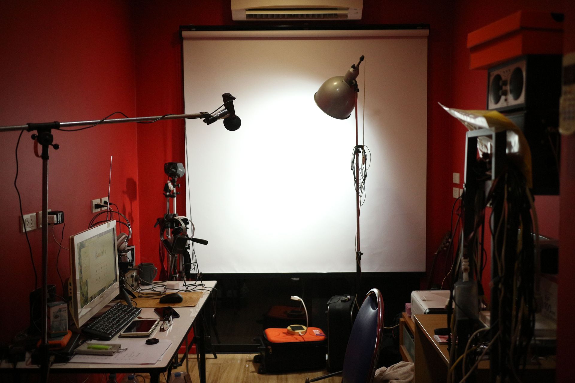 Red room with a desk, computer monitors, microphone boom, lamp, and bright white backdrop setup