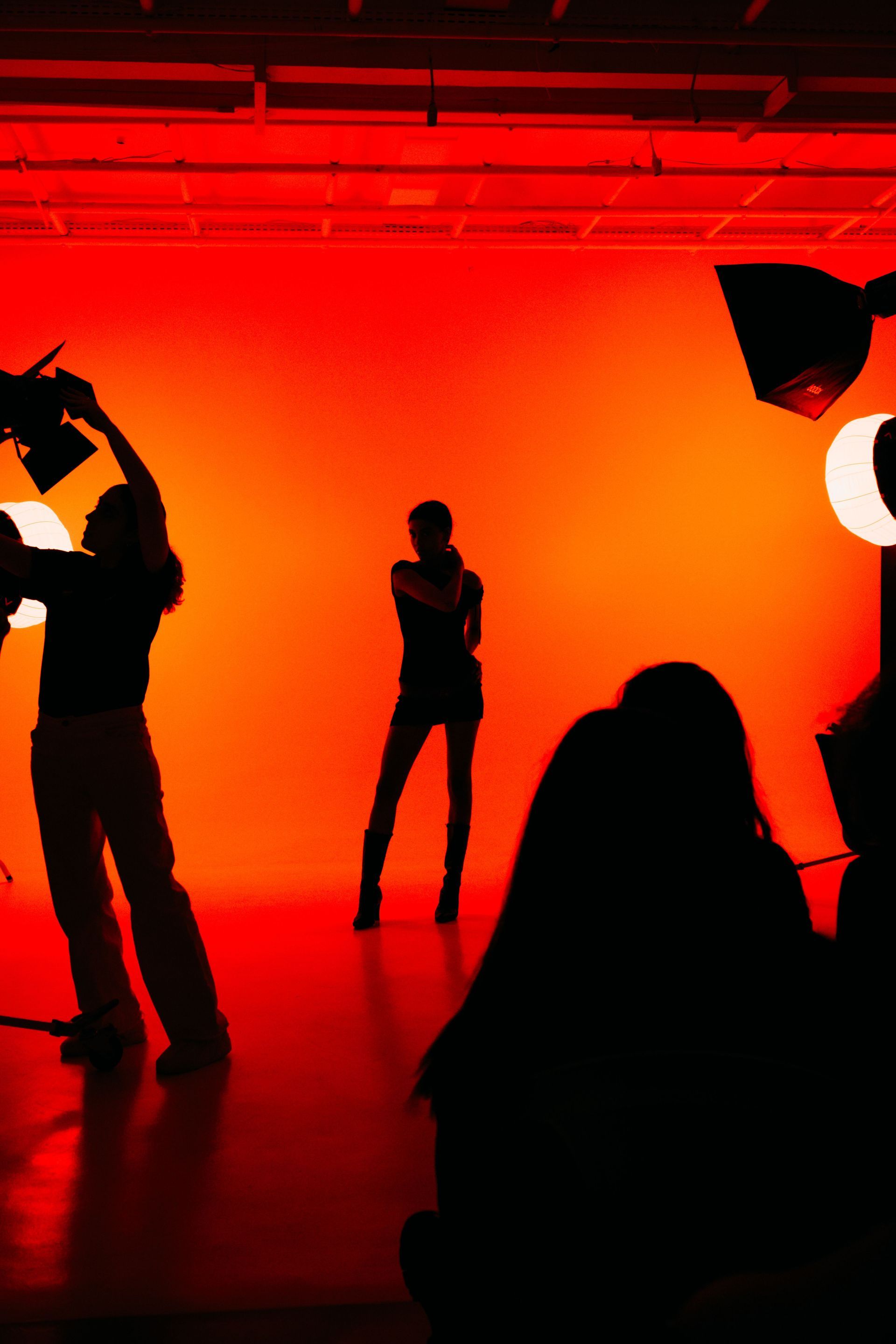 Silhouettes of people posing in a red-lit studio with a bright orange backdrop