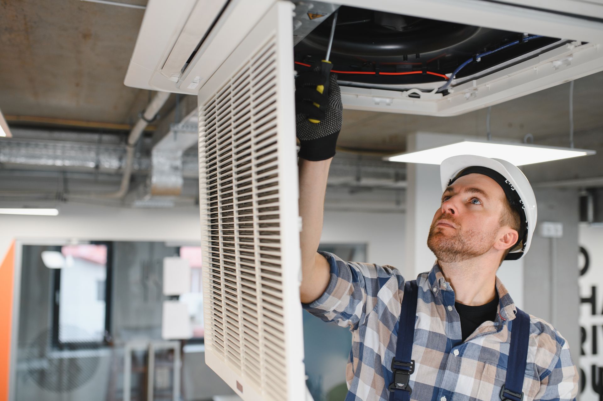 Technician inspecting a ceiling vent in an office, reaching up with tools.