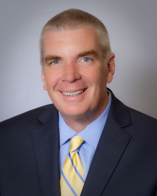 Man in suit and tie smiles, a professional headshot.