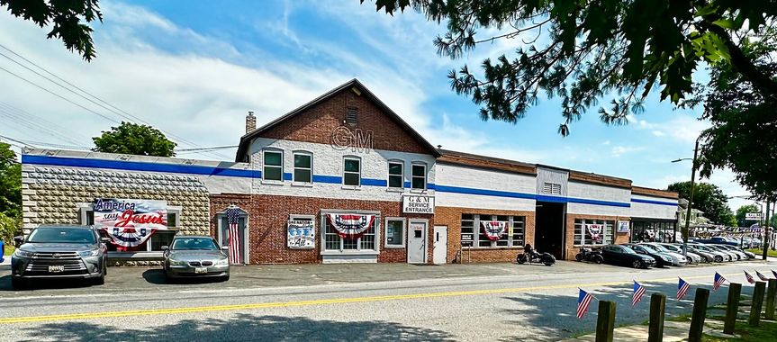 Street view of a storefront with brick facade, blue awnings, parked cars, and banners on a sunny day