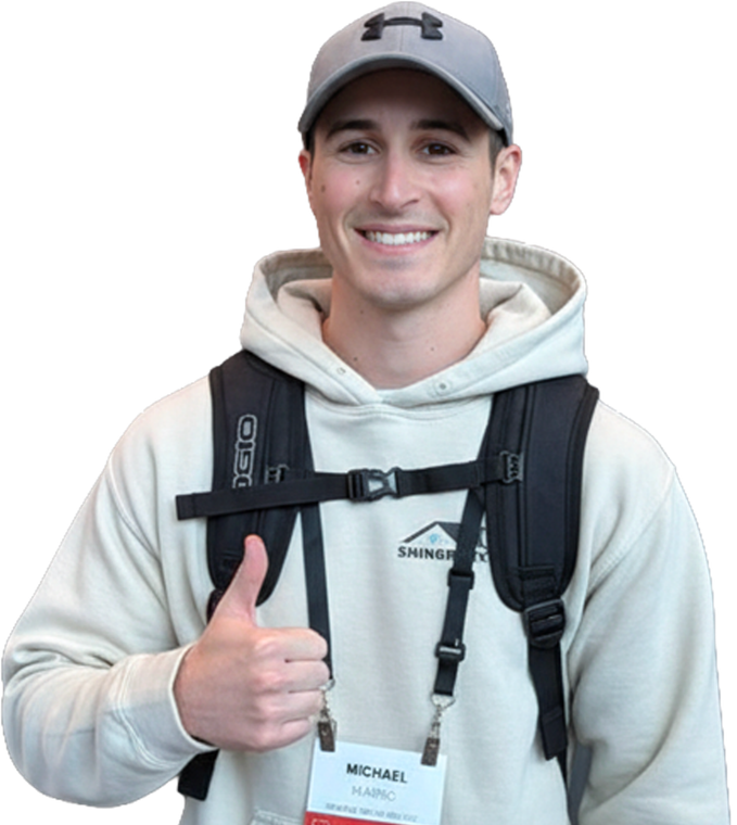 Smiling man in gray hoodie and cap giving a thumbs-up with backpack and name badge
