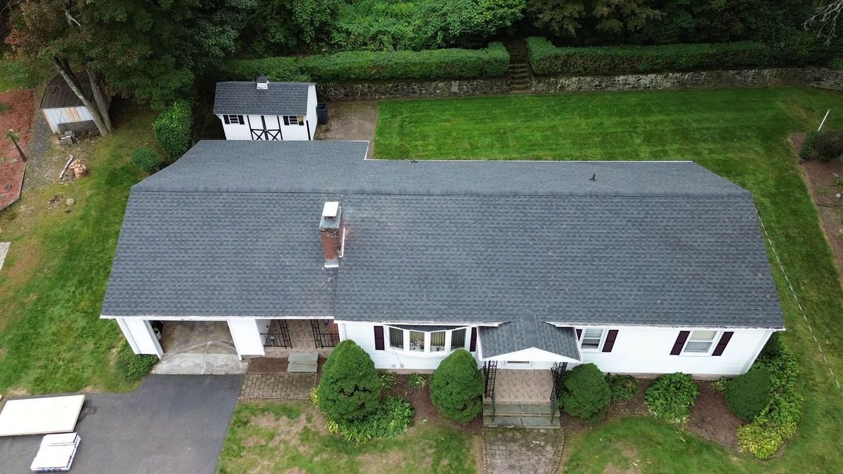 Roofing worker installing black shingles near a brick chimney on a sloped roof