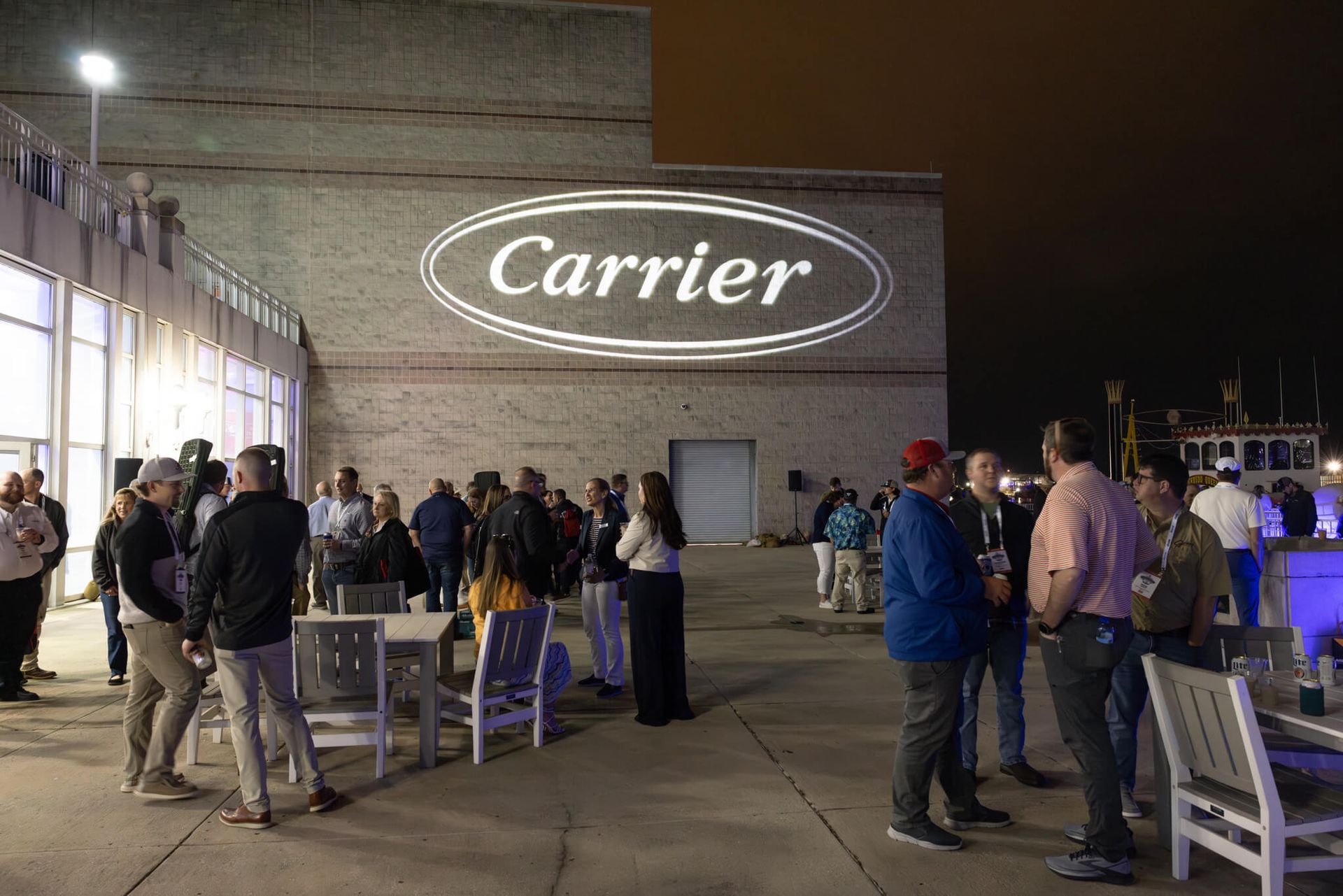 People gathered outside a Carrier building at night, with the illuminated logo on the wall.