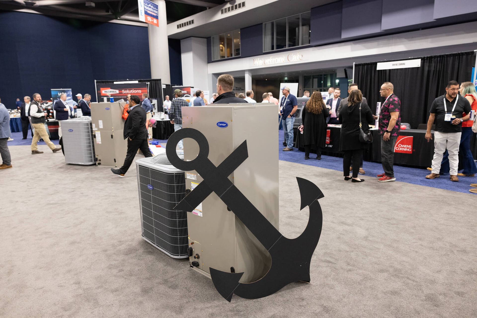 Large black anchor sculpture beside a gray display cube in a busy indoor convention hall