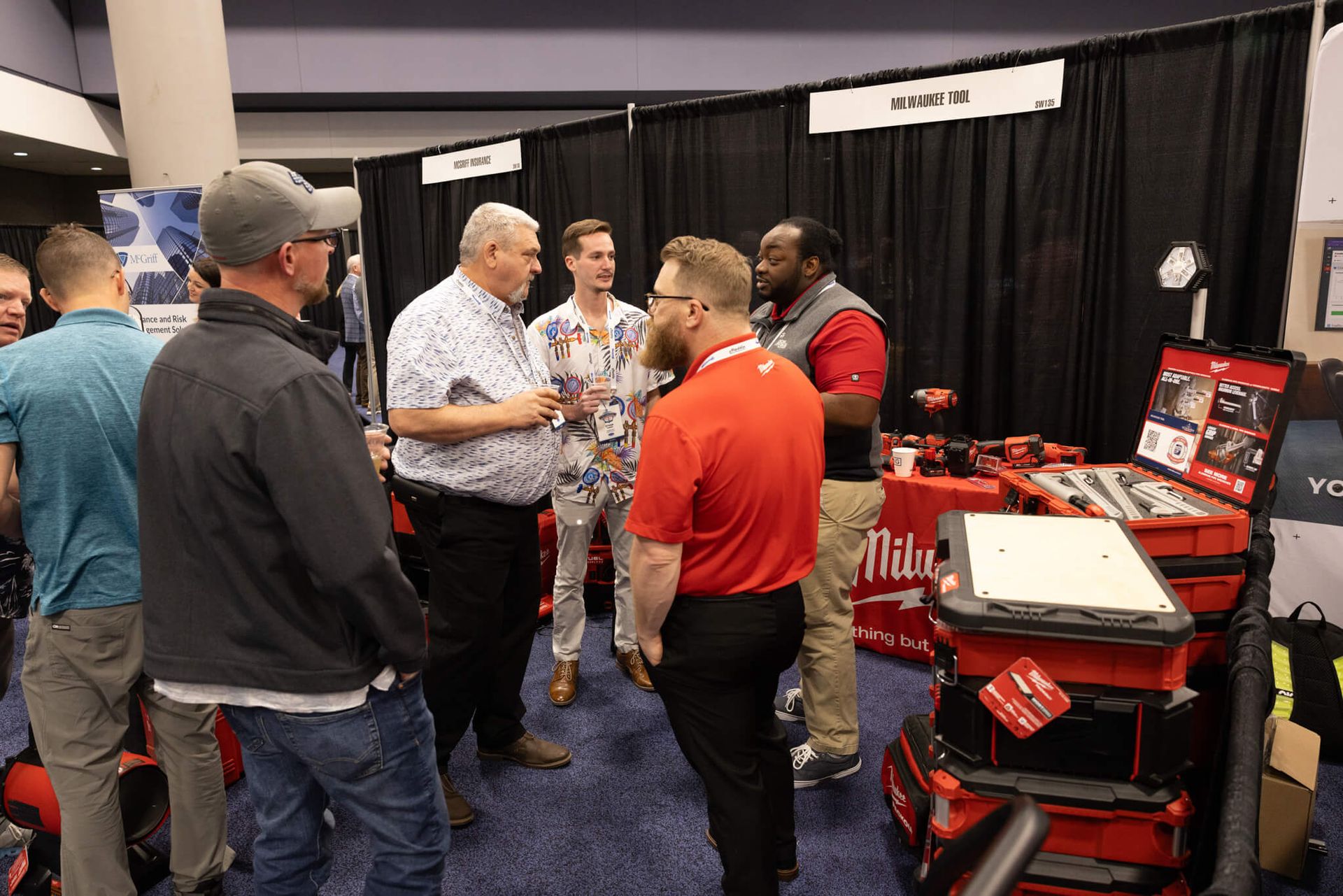 Trade show booth with several people talking beside red Milwaukee tool displays.