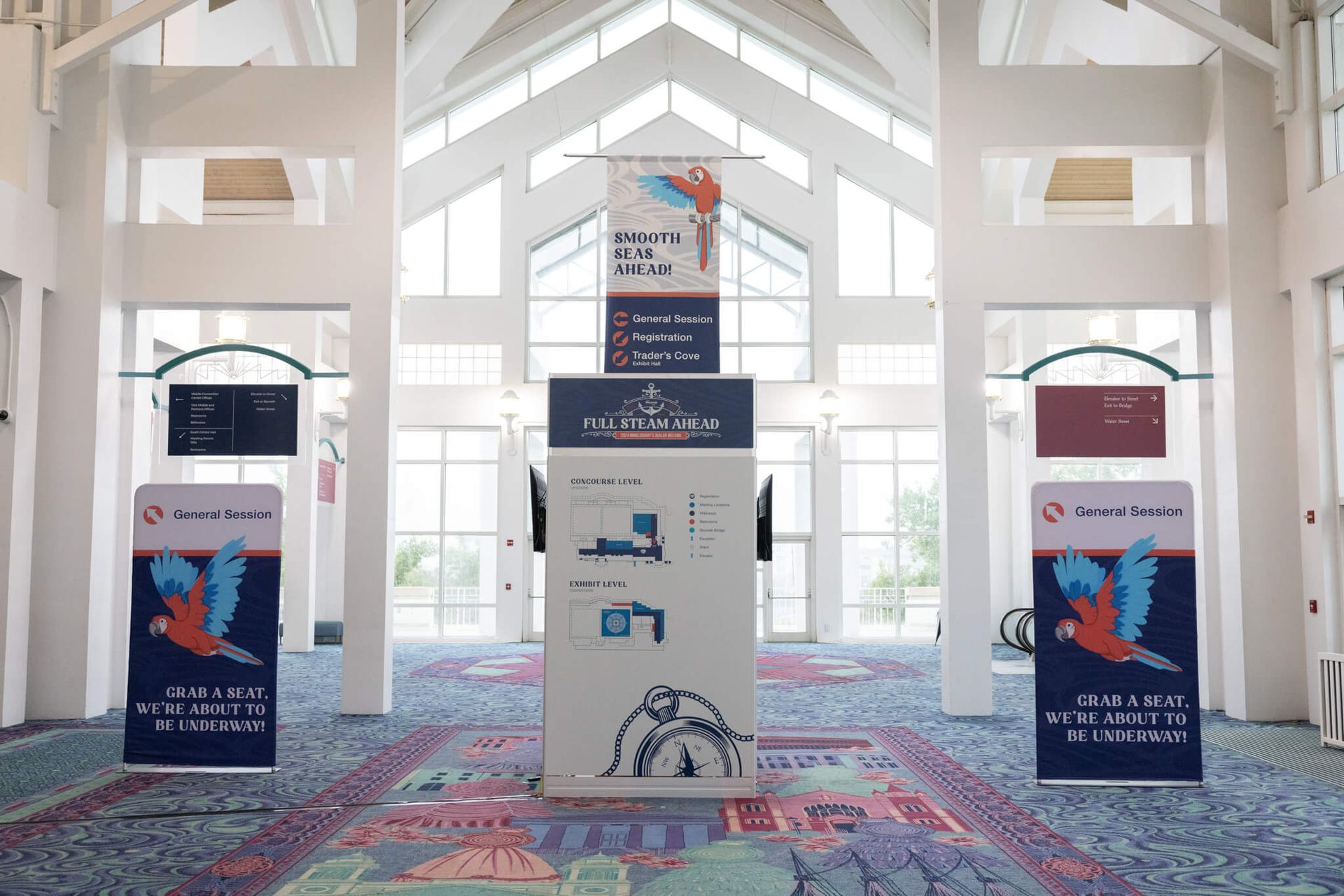 Bright lobby with a central display podium and four tall blue-and-red event banners on a patterned carpet.