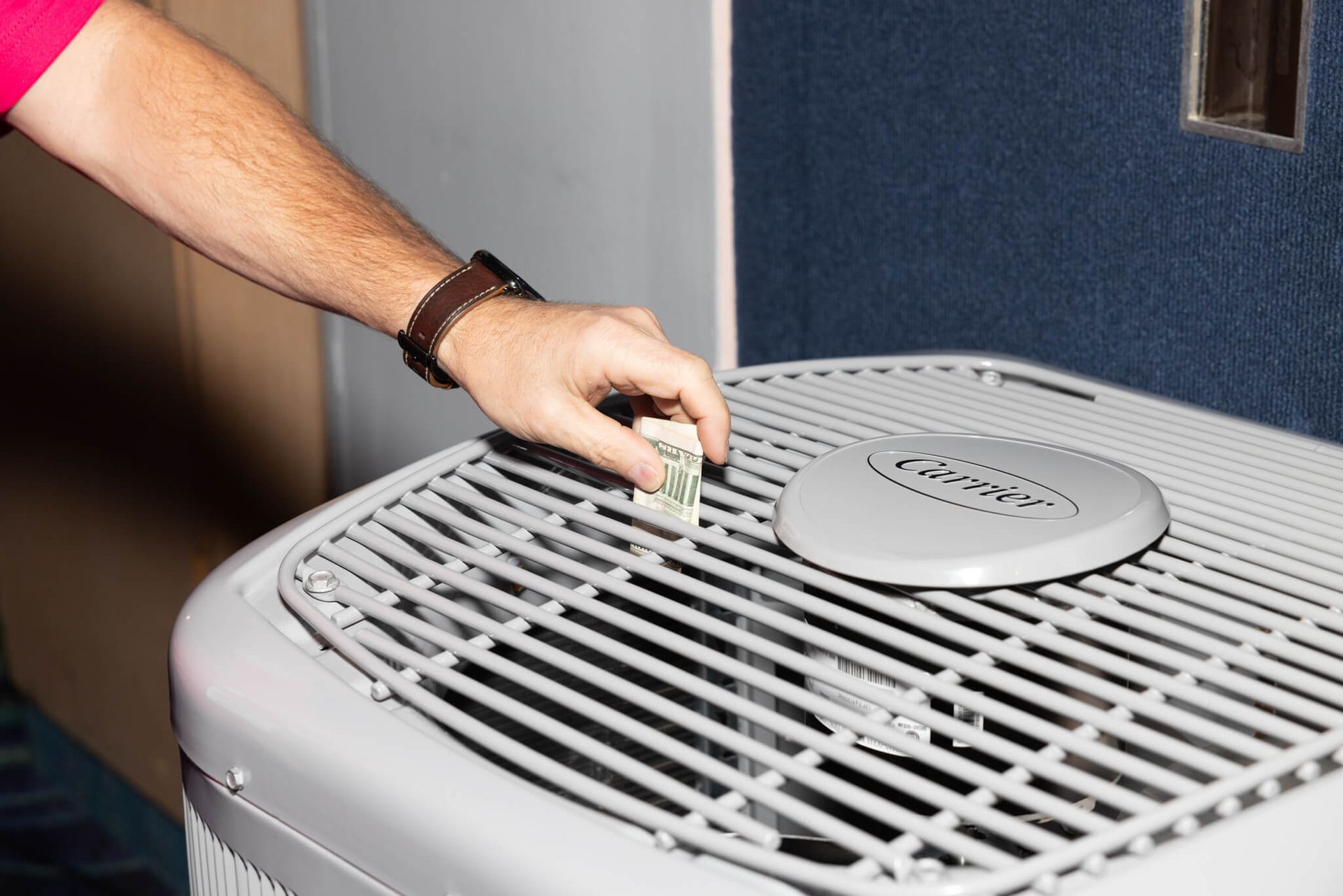 Hand placing a small component on a gray HVAC unit with a vented grille