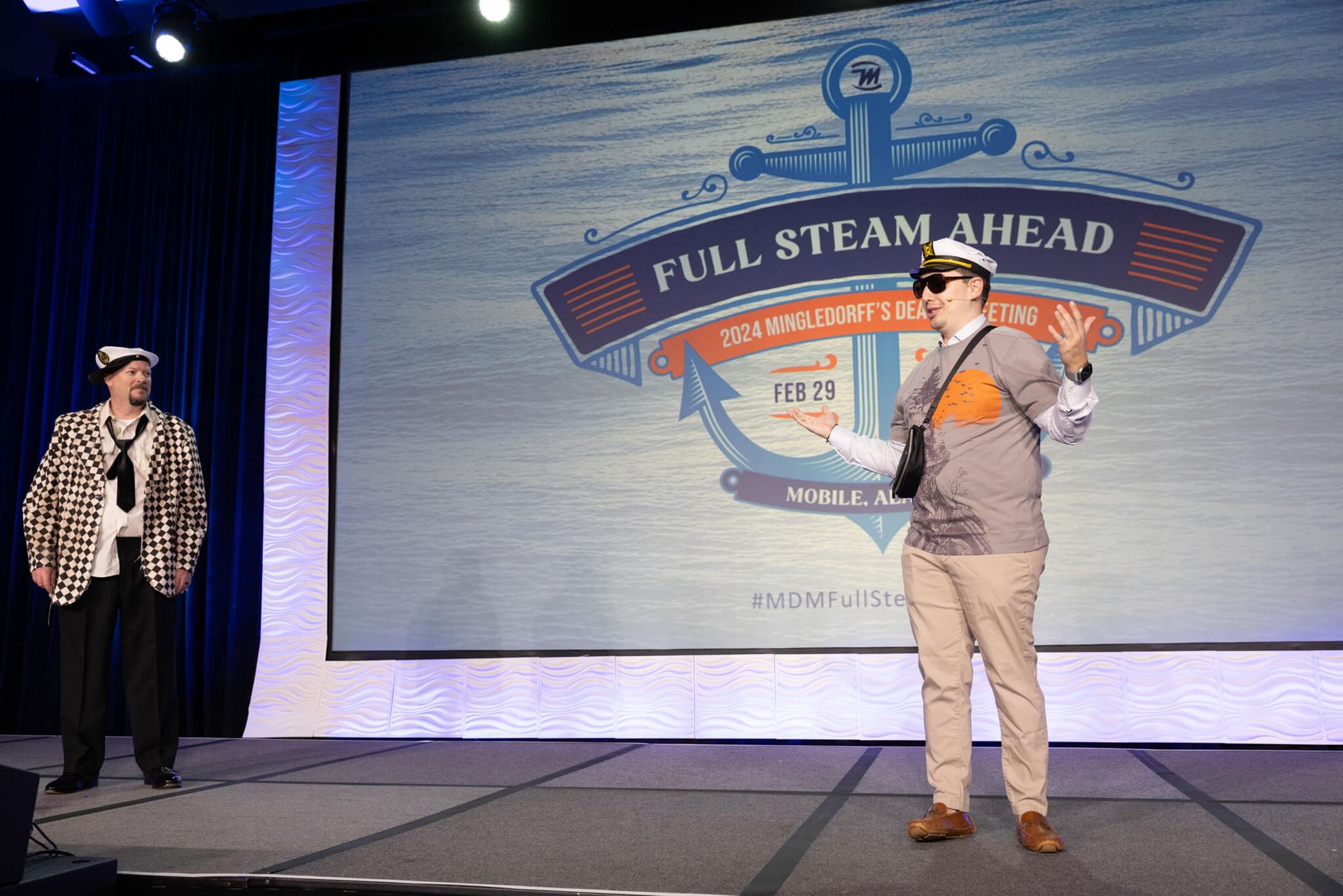 Two people on a stage before a “Full Steam Ahead” banner, one holding a microphone.