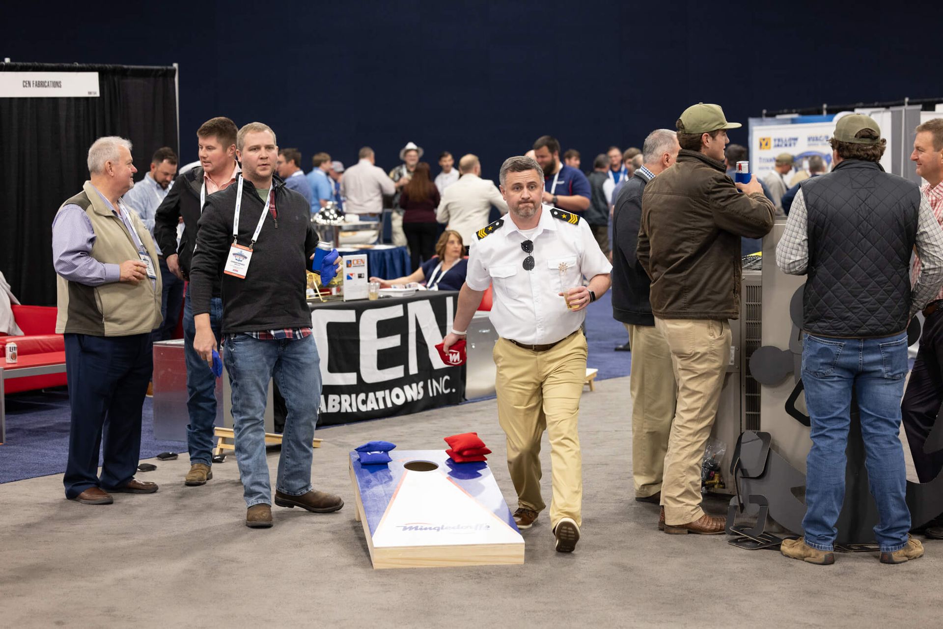 Indoor expo with people gathered around a booth and a man in a white shirt standing in front of a display.