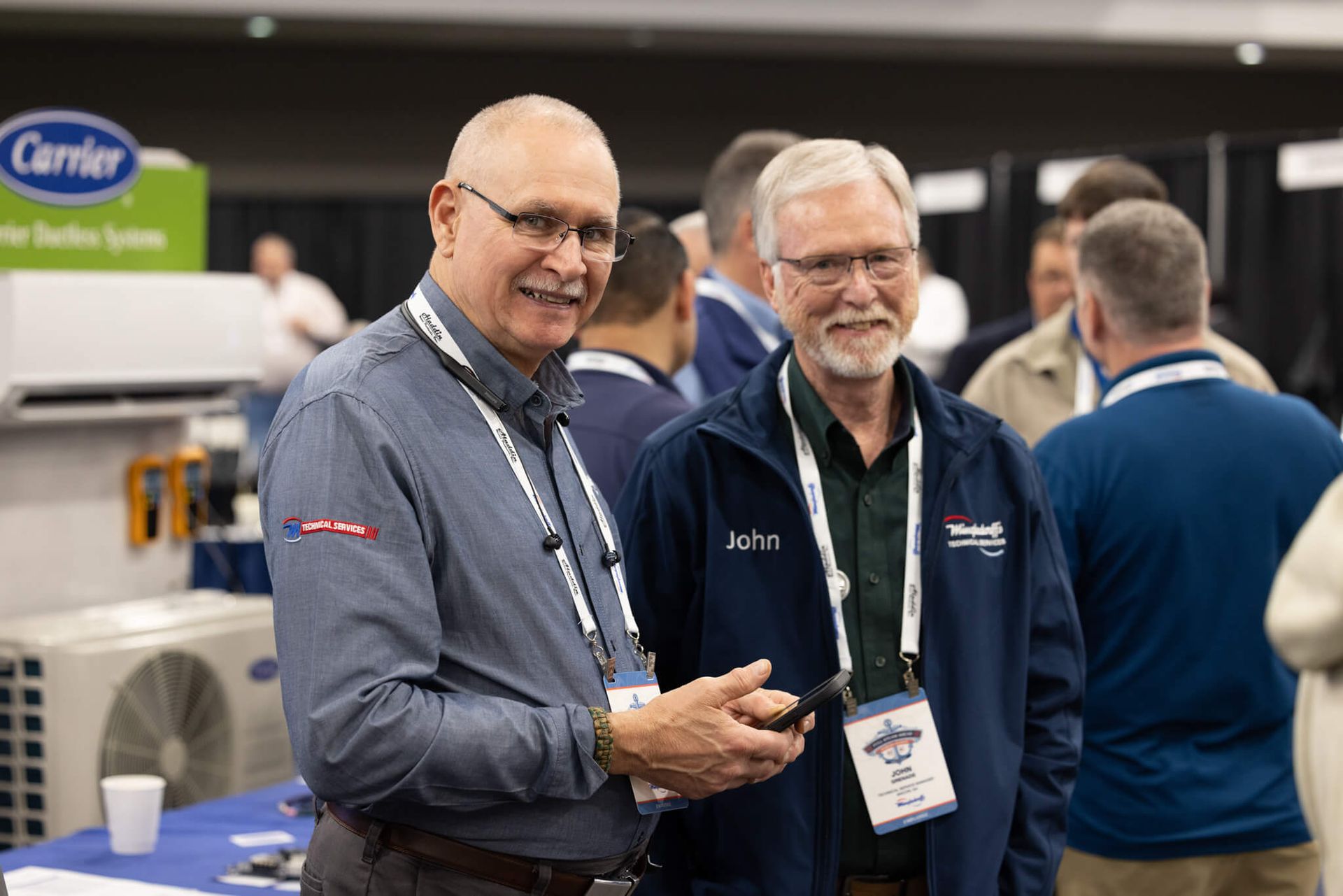 Two men in business attire smiling at a trade show booth with Carrier signage in the background