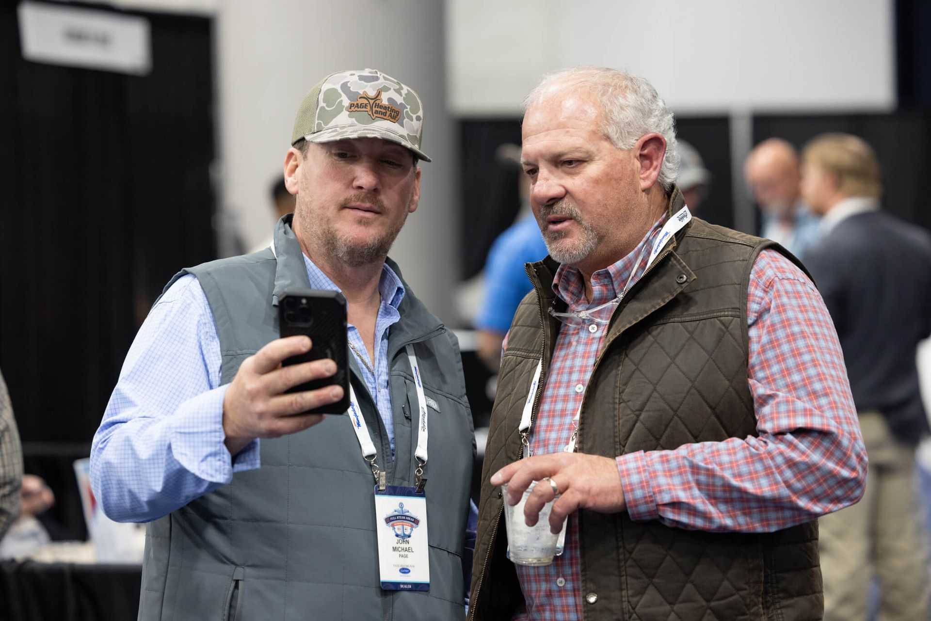 Two men at a conference looking at a smartphone, one holding a drink