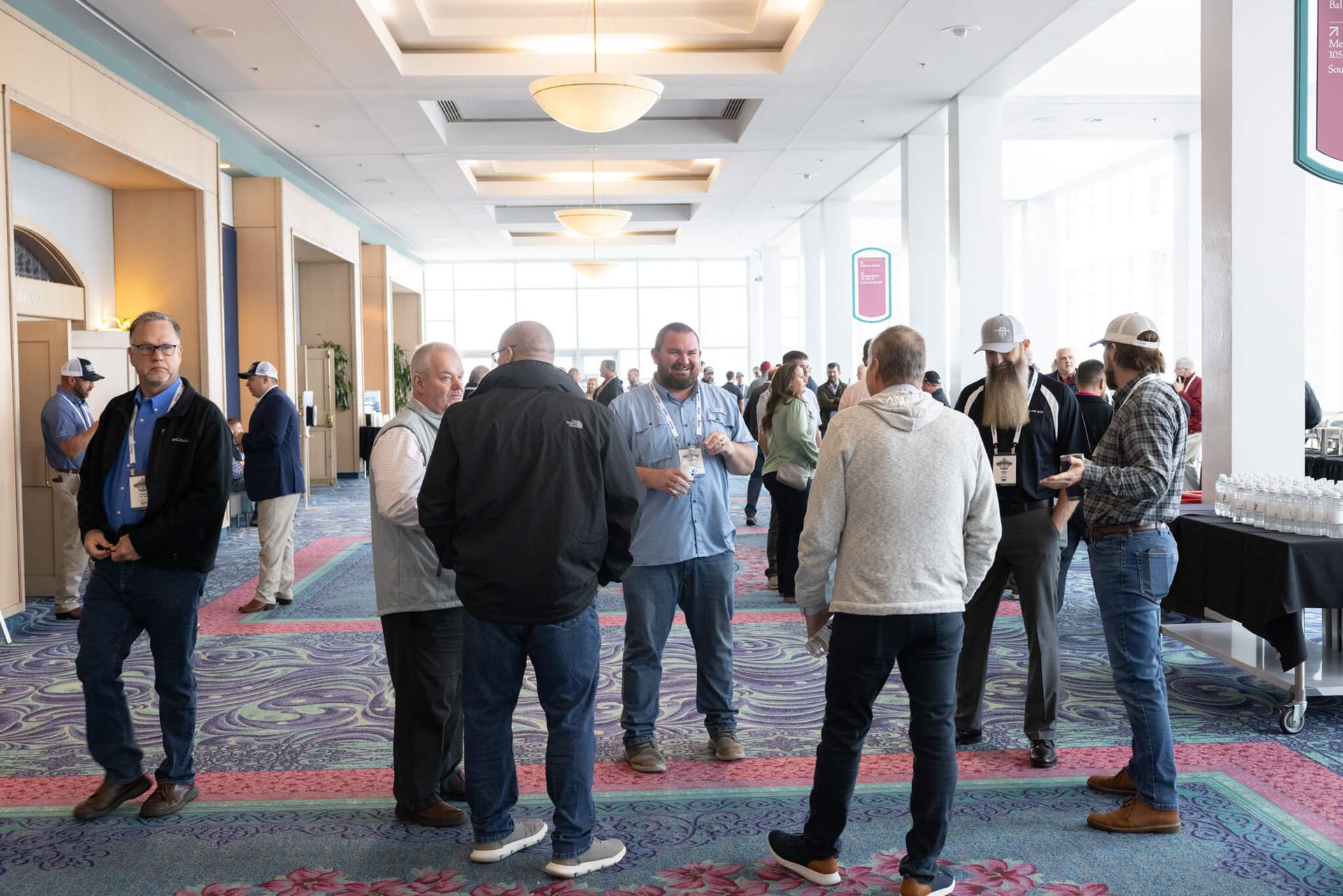 People gathered in a bright hotel hallway, standing and chatting on a patterned carpet.