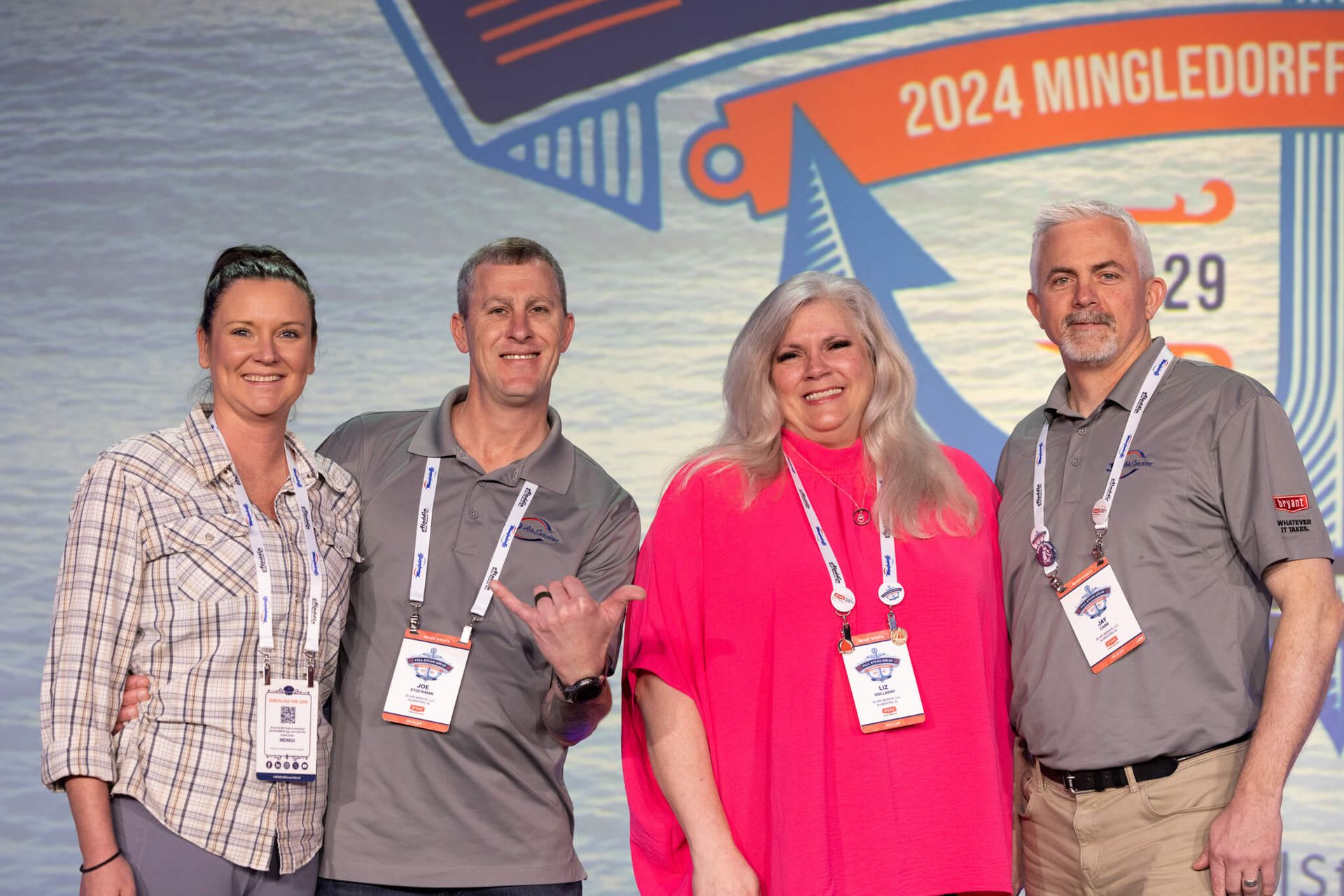Four people pose in front of a 2024 MingleDorf event banner, wearing conference lanyards.