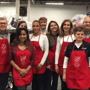 Group of volunteers in red aprons standing together and smiling in a kitchen or pantry setting
