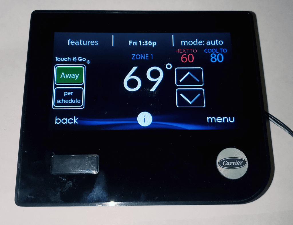 Black touchscreen thermostat showing 69° with up/down arrows and menu icons on a wall.