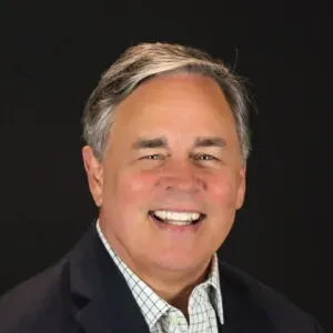 Smiling man in a dark suit and checkered shirt against a black background
