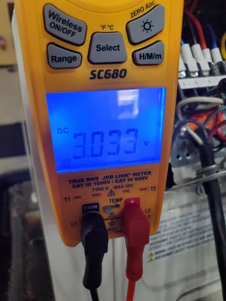 Blue-lit digital multimeter showing 3.033 V DC with black and red probes connected