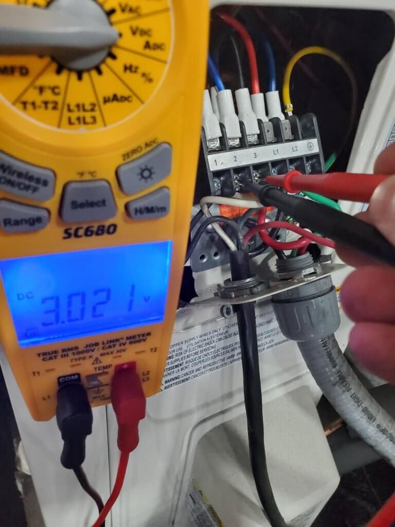 Digital multimeter showing 30.21 beside a wiring terminal block, with red and black test probes attached.